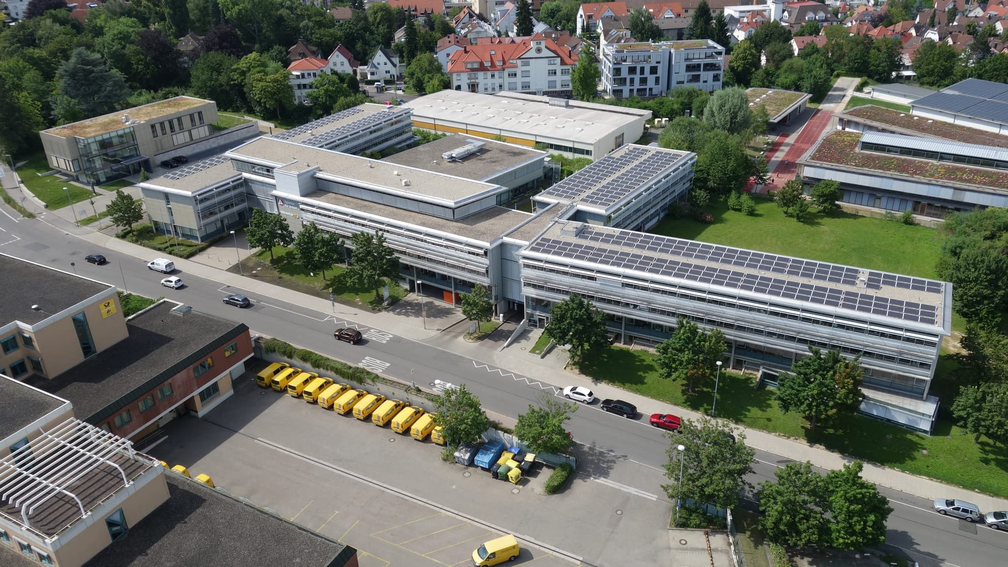 Die drei Flügel des Gebäudes im Zusammenhang, im Vordergrund das Postverteilzentrum mit gelben Fahrzeugen