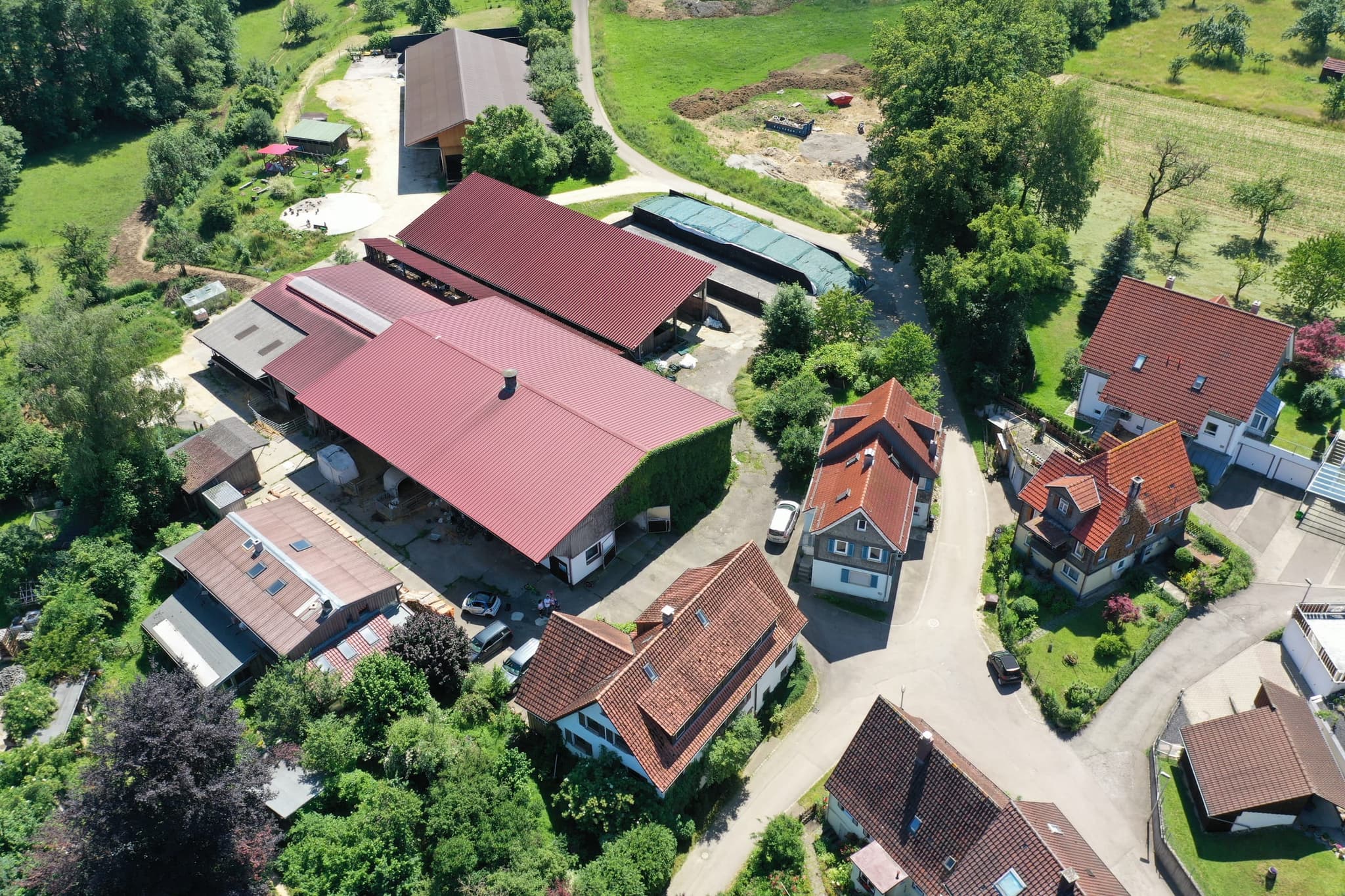 Die Hofstelle im Dorf, mit Wohnhäusern rundum und der Maschinenhalle am oberen Bildrand