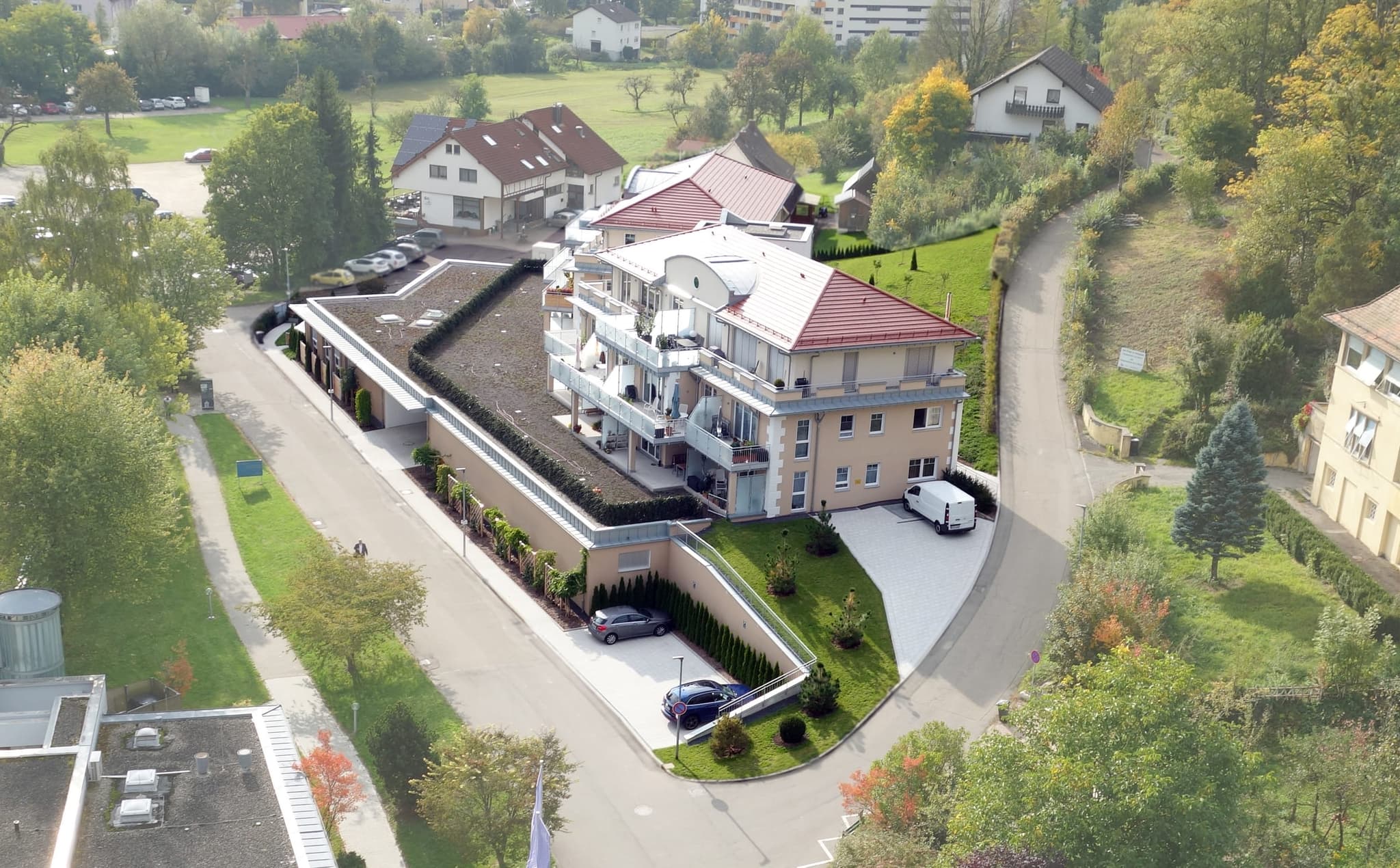 Dasselbe Haus von der Zufahrt aus, mit begrünter Tiefgarage, Hecke und den Streuobstwiesen am Ortsrand