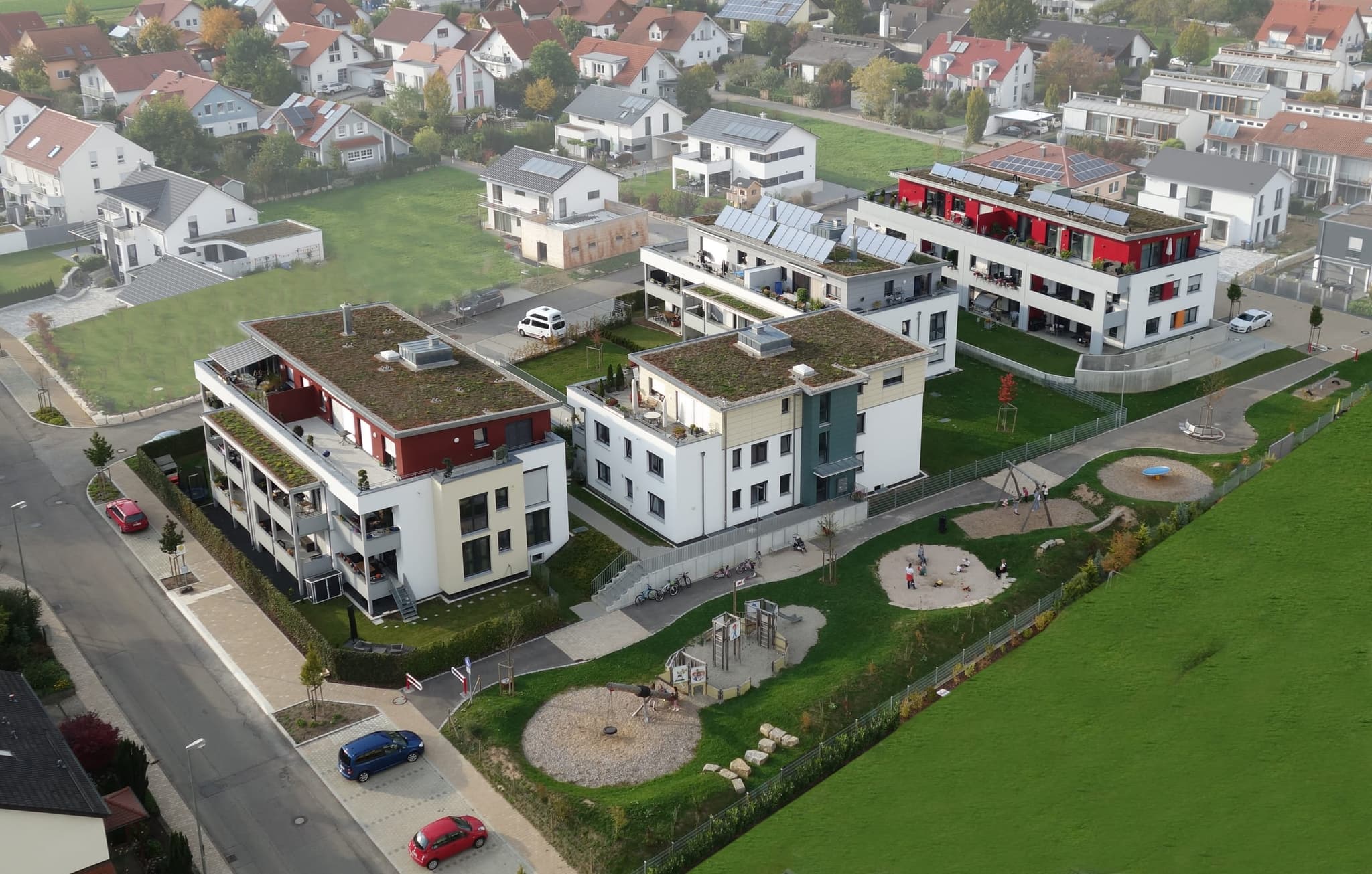 Blick von der Spielplatzseite: Sandflächen, Schaukel und Klettergerüst zwischen den Häusern