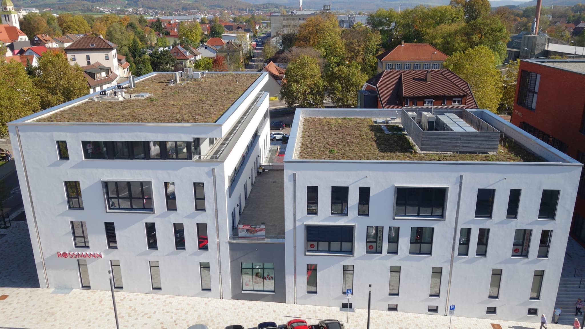 Nahaufnahme der beiden Bauteile mit der Passage dazwischen und den begrünten Dächern