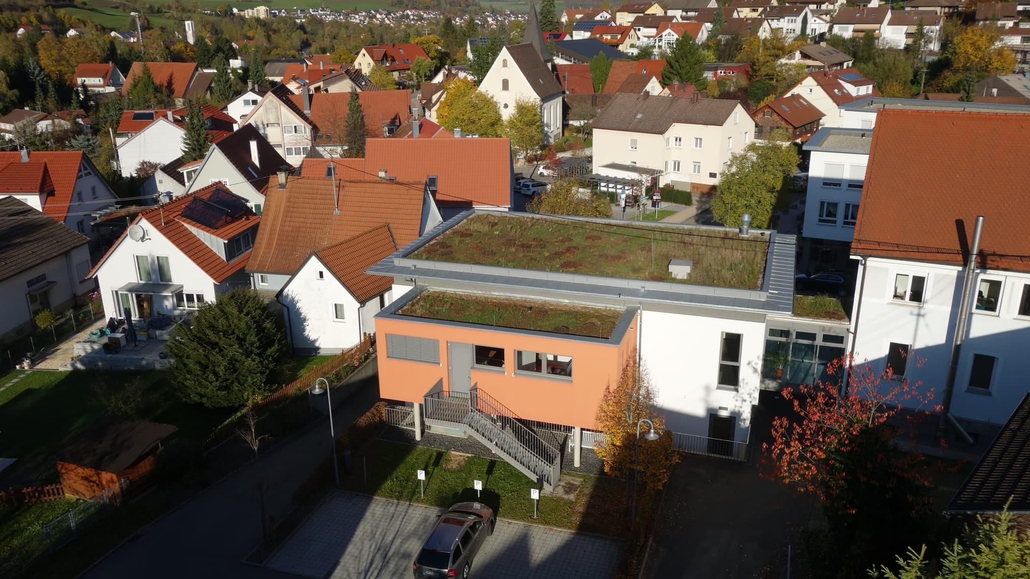 Rathausanbau Bad Ditzenbach: orange gefasster Baukörper auf Stützen, mit Außentreppe und Gründach
