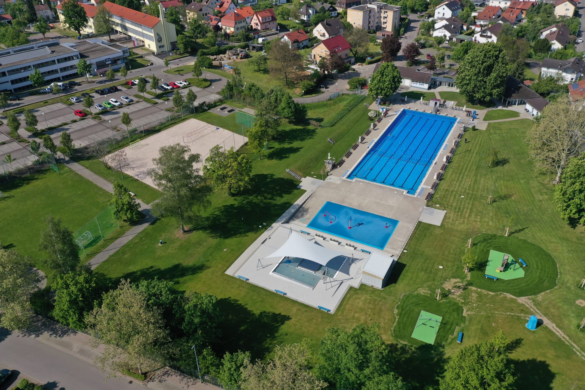 Die gesamte Anlage schräg von oben, mit Parkplatz, Beachfeld und Kinderbereich