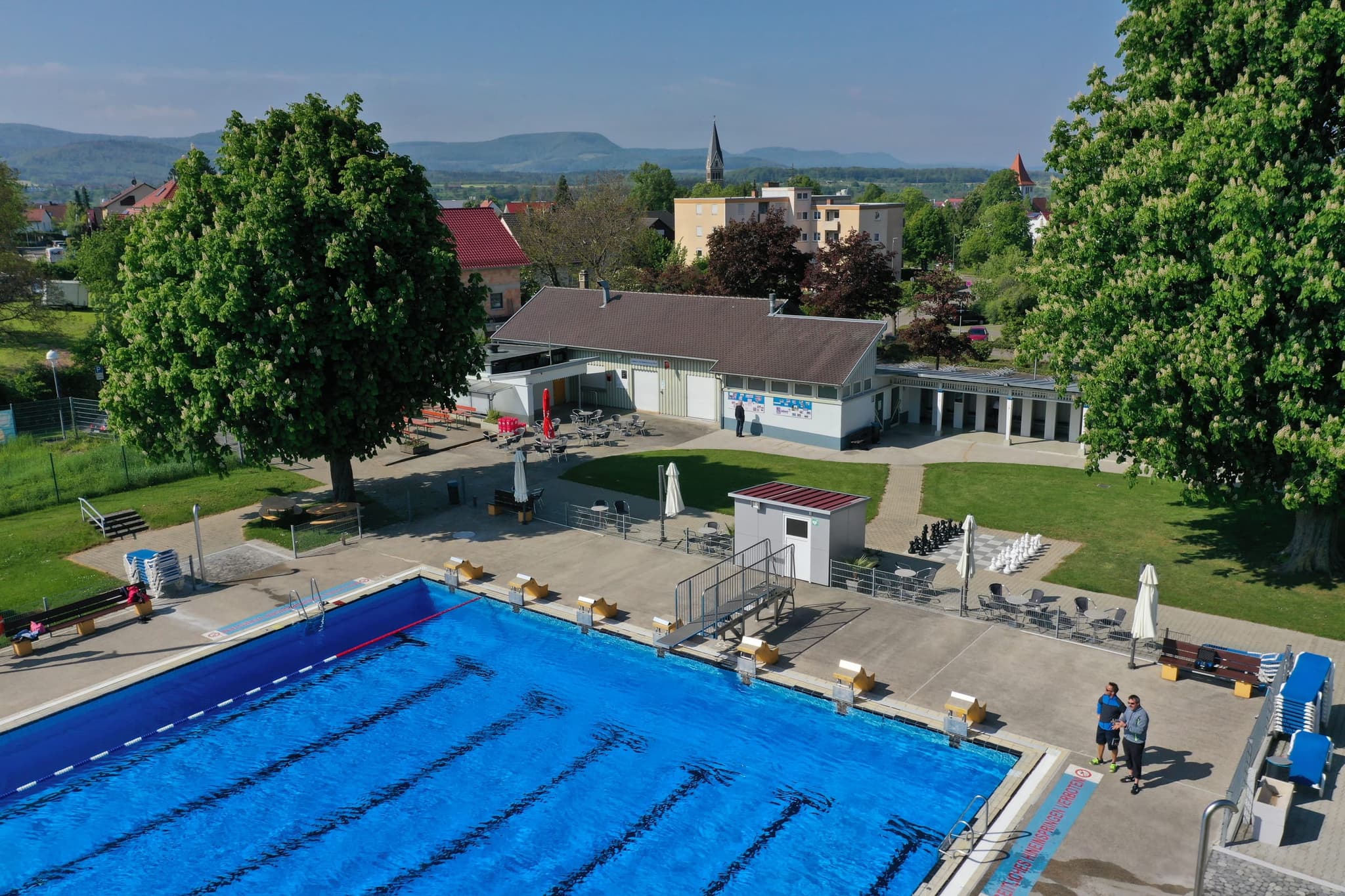 Beckenrand mit Startblöcken, Kassenhaus und Kastanien; hinten die Kirchturmspitze von Salach