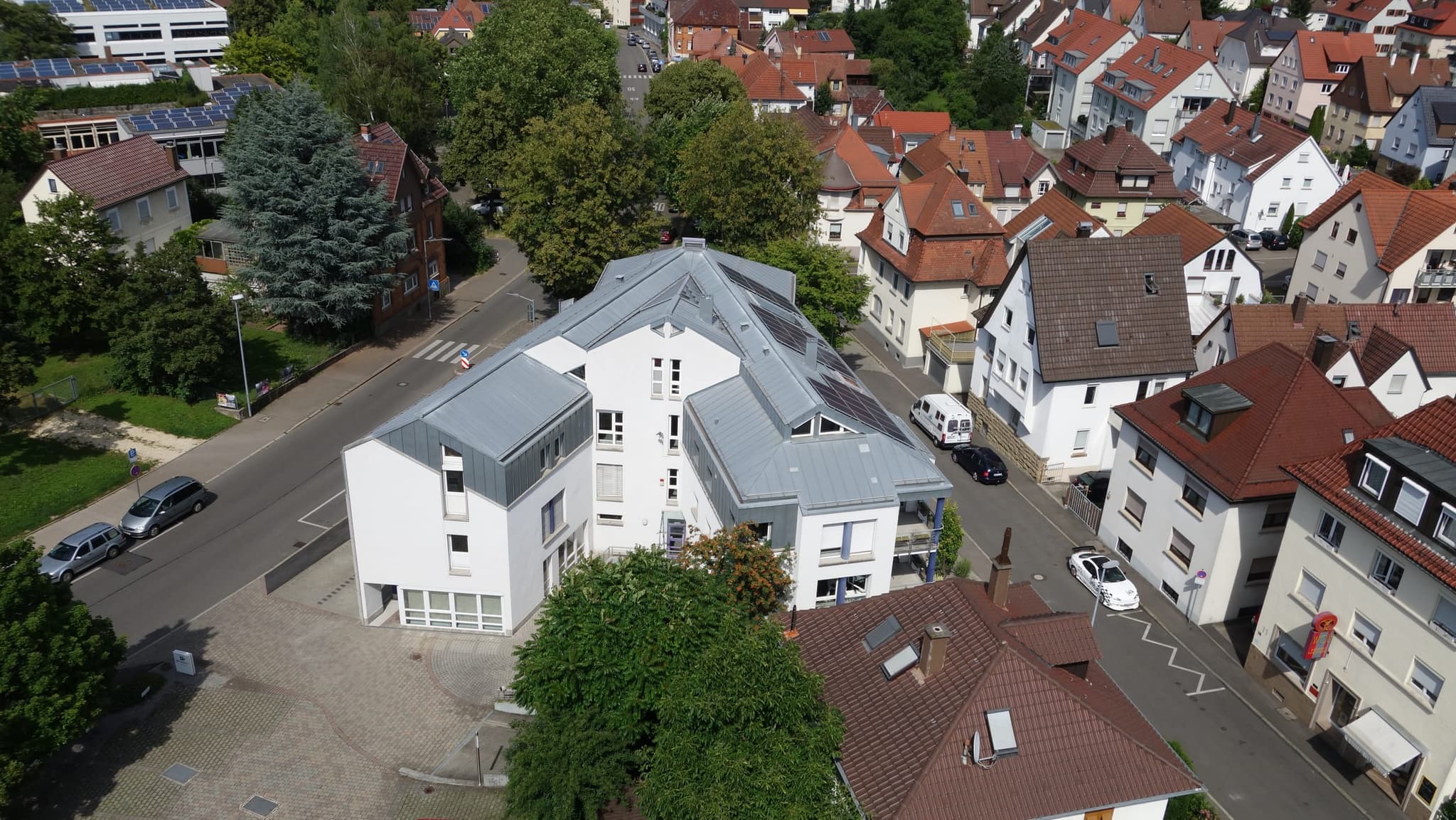 Derselbe Sitz von der anderen Straßenseite, mit Vorplatz, Solarfeld auf dem Dach und Altstadt ringsum