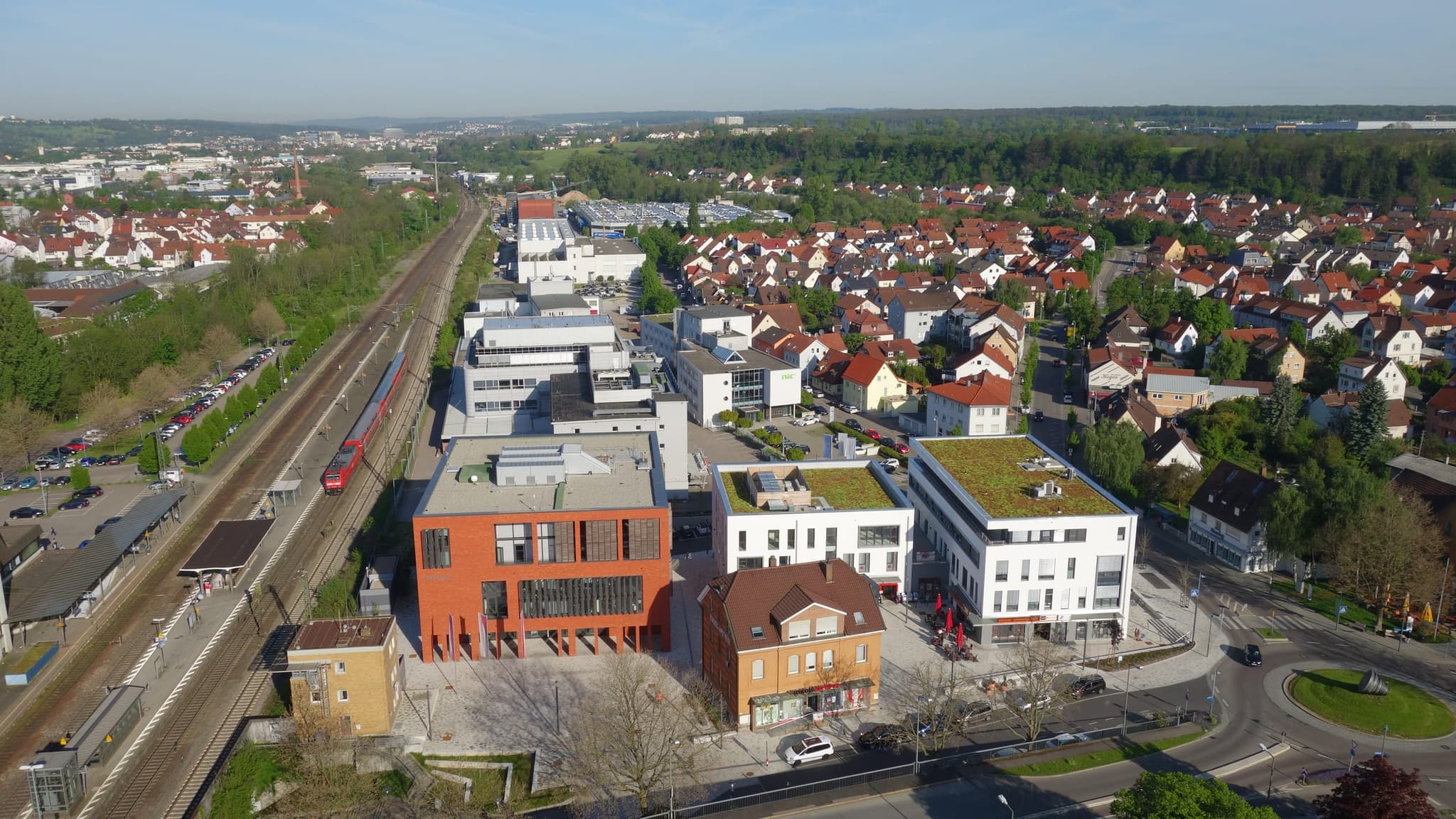 Rathaus, Bahnsteig und einfahrender Regionalzug in einem Bild, rechts der Kreisverkehr