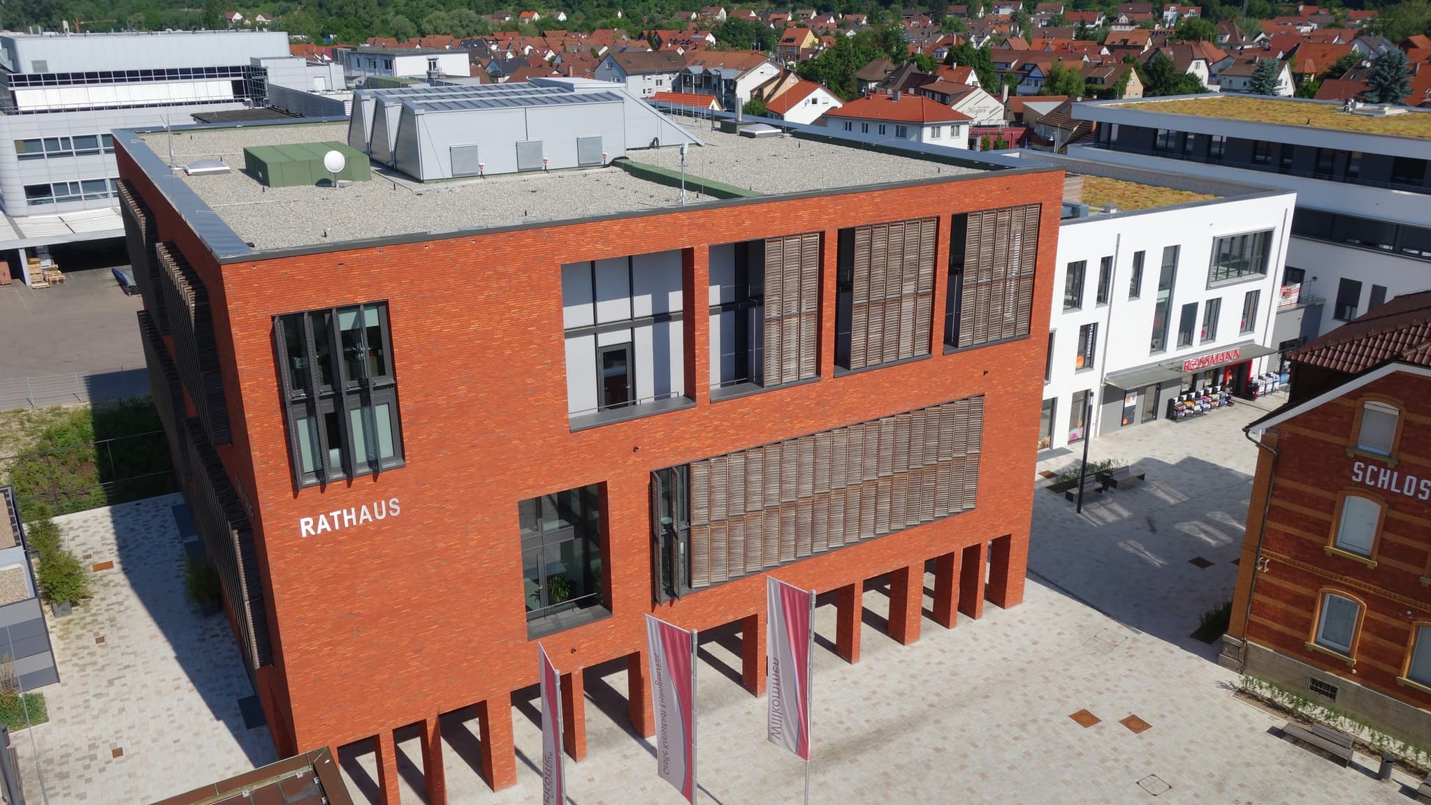 Nahaufnahme der Rathausfassade mit dem Schriftzug RATHAUS, Holzlamellen und Begrüßungsfahnen