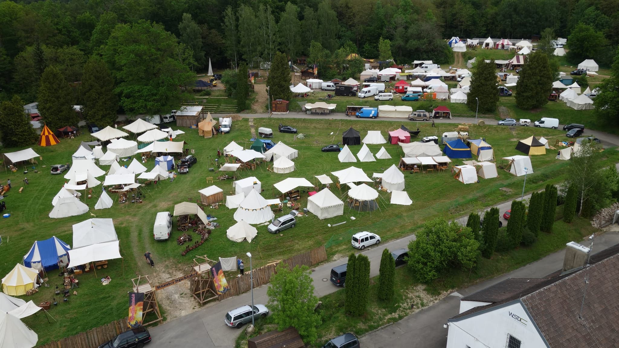 Das Zeltlager am Waldrand während des Aufbaus, mit Marktzelten und dem Eingangstor