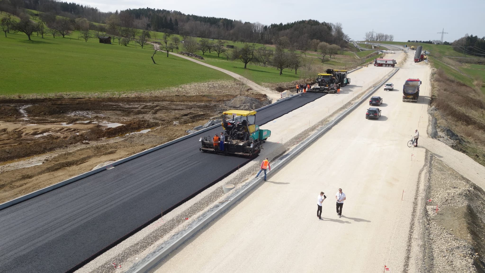 Der Asphaltfertiger zieht die schwarze Bahn, rechts die noch ungebundene Tragschicht