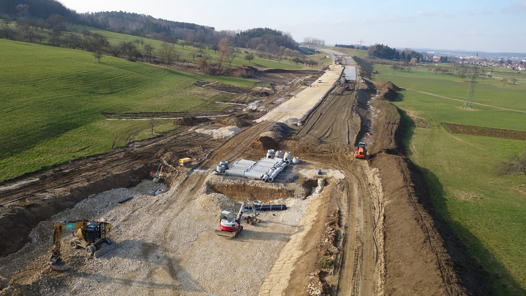 Kanalbau in der Trasse, mit Betonrohren, Bagger und Walze auf dem Planum